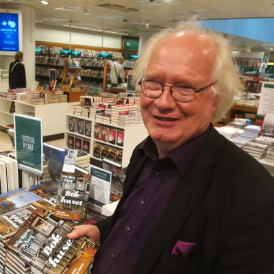 Författaren Stig-Björn Nyberg står bredvid en hög med böcker. 
