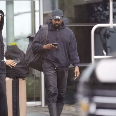 Kanye West iklädd keps med trycket 2023 och en telefon i handen.