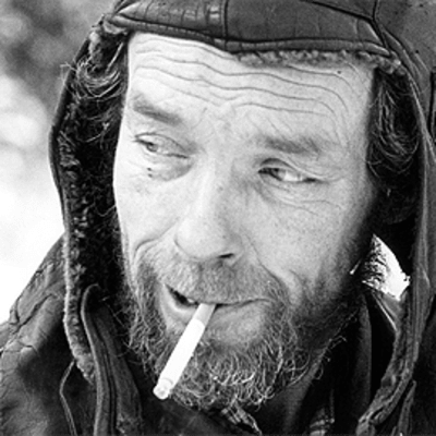 Kasvokuva miehestä metsätöissä talvella. Tupakka suussa.
