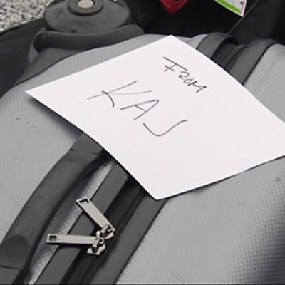 Matkalaukku, jonka päällä käsin kirjoitettu lappu "from KAJ"