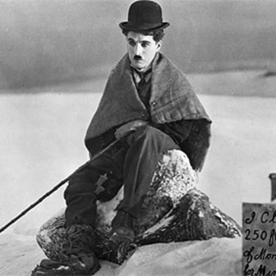 Charles Chaplinin kulkurihahmo istuu lumessa, vierassä kyltti kertoo hänen vallanneen maata kaivosta varten.