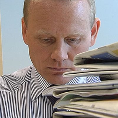 AKT:n puheenjohtaja Timo Räty työpöytänsä ääressä. Edessään korkea pino lehtiä.