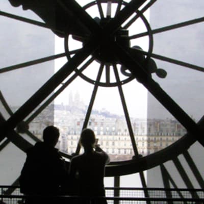 Kaksi henkilöä seisoo valtavan kellon alla d'Orsayn museossa Pariisissa.