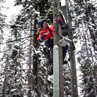 Sähkölaitoksen työntekijä kiipeää sähkötolppaan lumisessa metsässä.