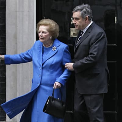 Gordon Brown pitää kiinni Margaret Thatcheristä, joka pitää toisella kädellään kiinni rautaportista.