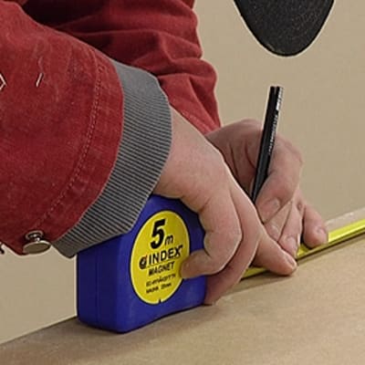 Rakennusmies mittaa levyä mittanauhalla ja tekee merkintää levyyn.