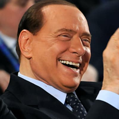 Italian pääministeri Silvio Berlusconi nauraa ja taputtaa käsiään konferenssin yleisössä.