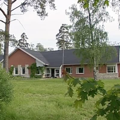 Vanhainkodin rakennus ja pihaa: matala harjakattoinen rakennus, puita ja pensaita.