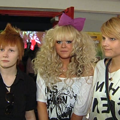 Kolme k-pop tyylin mukaisesti pukeutunutta tyttöä. Keskimmäisellä fuksian punainen suuri rusetti hiuksissaan.