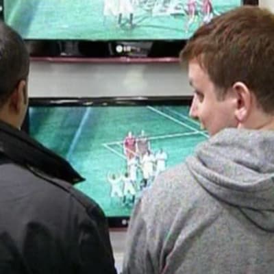 Kaksi nuorta miestä kokeilee FIFA 11 -jalkapallopeliä liikkeessä.