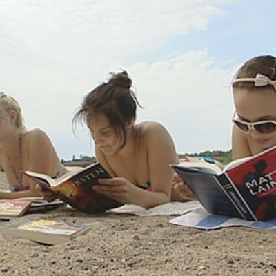 Kolme tyttöä lukee rannalla
