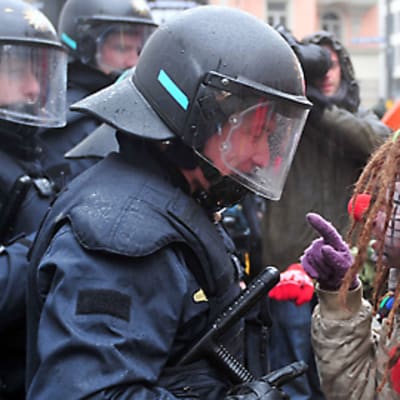 Klovniksi pukeutunut mielenosittaja keskustelee mellakkavarusteisen poliisin kanssa Münchenissä helmikuussa 2010
