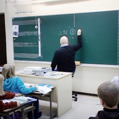 Alakoulun opettaja kirjoittaa liitutaululle luokkahuoneessa.