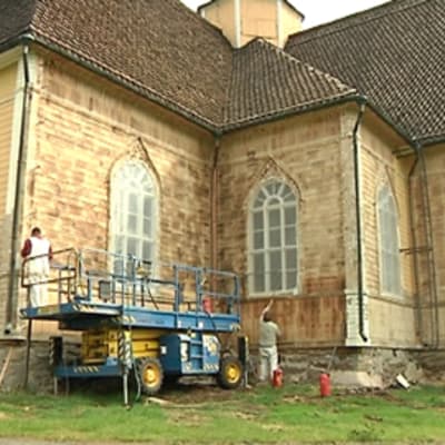 Kaksi miestä poistamassa maalia Lohtajan kirkon ulkoseinästä kirkon kunnostustöiden yhteydessä.