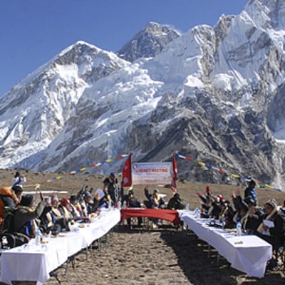 Nepalin pääministeri johtaa hallituksensa istuntoa ulkoilmassa Kalapatharissa Mount Everest -vuoren juurella. Aurinkoinen sää. Pöydillä valkeat pöytäliinat.