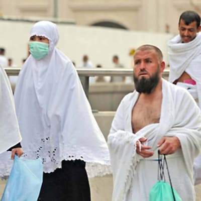 Kolme naista on pukeutunut burkhaan ja hengityssuojaimiin. Kaksi oikealla olevaa miestä kulkevat ilman suojaimia.