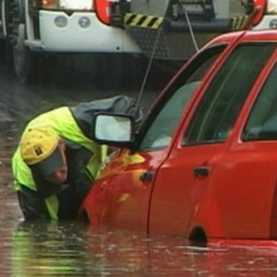 Mies työntää puolittain vedessä olevaa autoa.