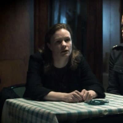 Kerttu Nuortevaa esittävä Minna Haapkylä istuu pöydän ääressä ja tuijottaa eteensä vierellään kuulustelija Paavo Kastaria esittävä Marcus Groth.