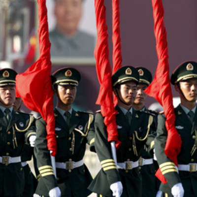 Joukko sotilaita kantaa ylväästi Kiinan lippuja olkapäillään.