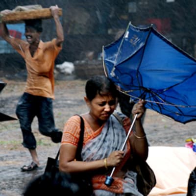 Nainen pitelee kiinni sateenvarjosta myrskyn keskellä Kalkutassa.