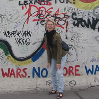 Reppuselkäinen Anna Korolainen Berliinin muurilla, muurin graffiteissa sanotaan mm. "No more wars. No more walls."