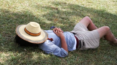 Man som ligger på gräset med en hatt över ansiktet.