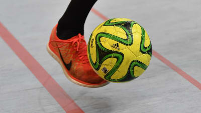 Person med orange gymnastisko sparkar gul futsalboll.