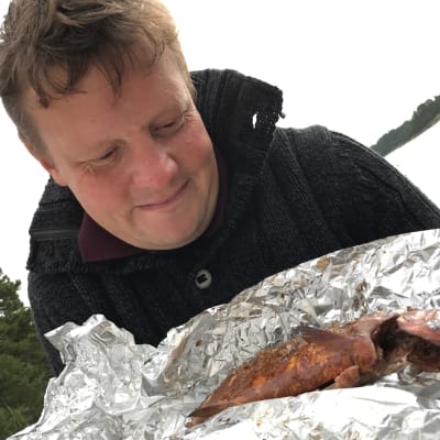 Michael Björklund står och tittar på en rökt sik som ligger i en bit med folie.