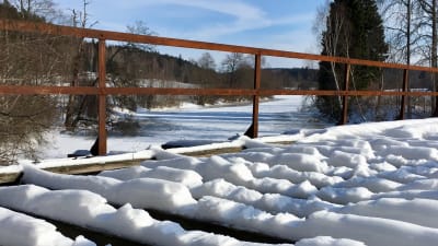 Sliten gammal snöbeklädd järnvägsbro i trä över ett vattendrag en vinterdag.