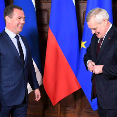Dmitrij Medvedev och Antti Rinne, bägge klädda i mörk kostym, står framför ett antal flaggor. 