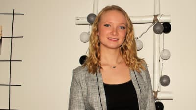 Michelle Ena har en grå kavaj på sig och står framför en vit vägg.
