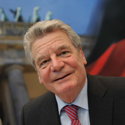 Joachim Gauck, en gråhårig leende man, framför en tysk flagga.