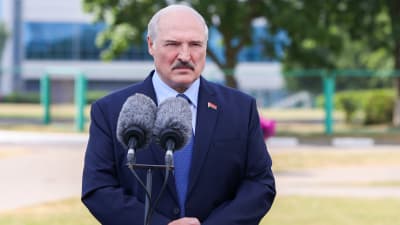Aleksandr Lukasjenko framför mikrofoner då han talar efter röstning i val. Han har lite ljust, grått. Mörk mustasch och mörkblå kavaj. Ser sammanbiten ut.
