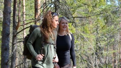 Marina och Lina går i en grön skog med ryggväskor.