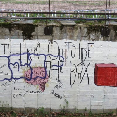 Graffiti på en vit tegelvägg. Det står "Think outside the box" plus några förnamn. 