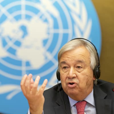 Antonio Guterres med handen i vädret, i bakgrunden FN-logon.