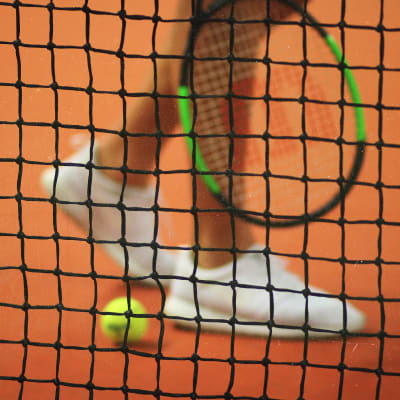 Närbild på en person med tennisskor och tennisracket.