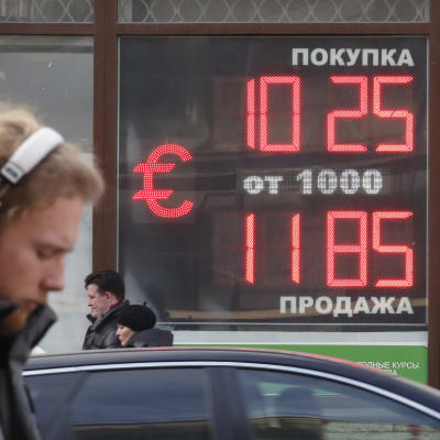 En digital tavla visar rubelkursen mot euron. En man med hörlurar i förgrunden.