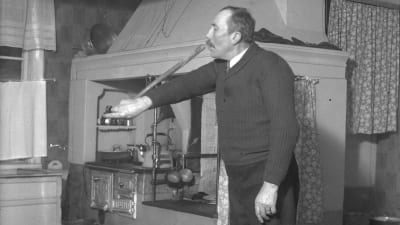 En man leker leken "pussa käppen", där han kysser ändan av en käpp som han håller i ena handen. Bilden är tagen 1938 i Närpes, Näsby.