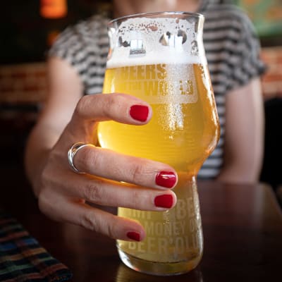 En kvinna , man ser en hand med röda naglar inget mer, håller i ett ölstop på en restaurang.