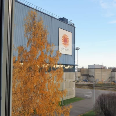 Stora Enson tehdasalue kuvattuna ikkunasta. Etualala sininen tehdasrakennus, jonka seinässä Stora Enson logo.