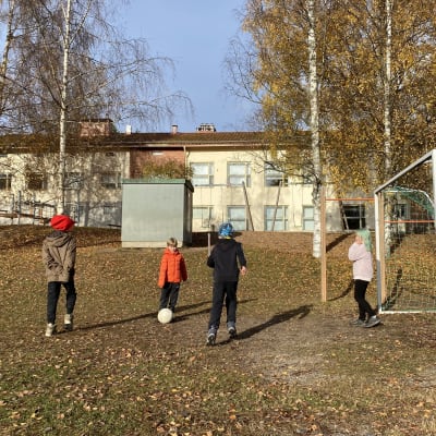 Koululaisia pelaamassa jalkapalloa pihalla. 