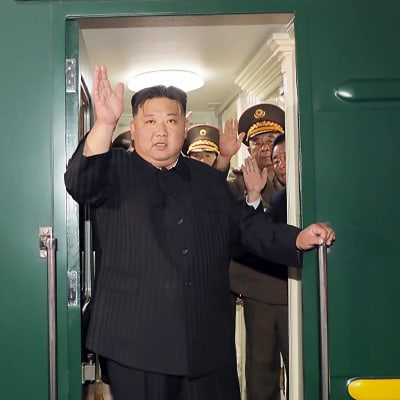 Kim Jong-un seisoo junan ovella ja heilauttaa kättään.