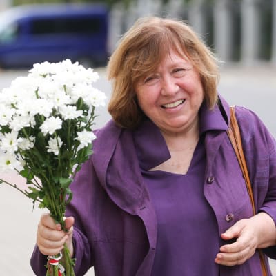 Kvinna klädd i lila står med vit blombukett i handen.