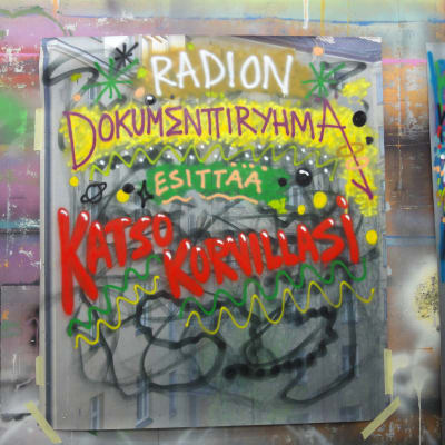 Värikäs graffiti, jossa lukee "Radion dokumenttiryhmä esittää katso korvillasi"