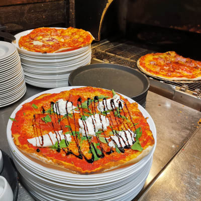 Pizza tulossa uunista, etualalla näkyy Pizzeria Napolin Burrata-pizza.