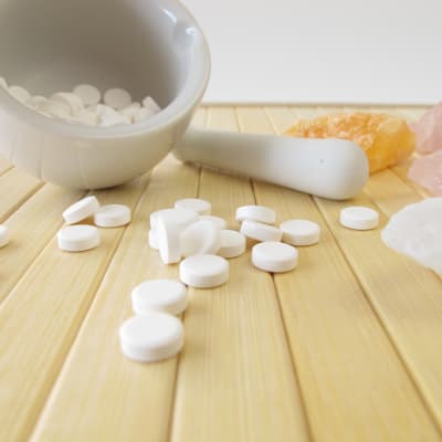 En mortel med vita tabletter, piller i. Rosenstenar, kvartsstenar syns också.