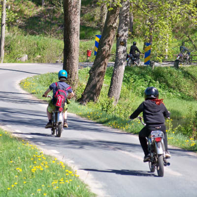 Mopedister kör efter varandra på en asfalterad väg.