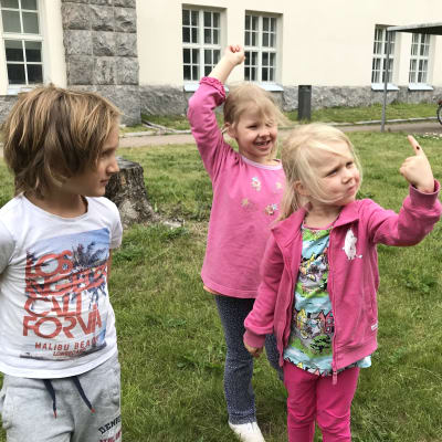 Flicka håller upp nyckelpiga på sitt pekfinger, två andra barn ser på.