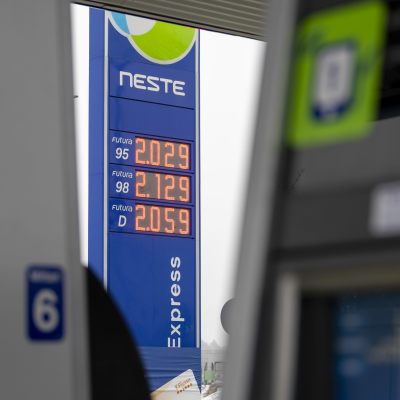 Stolpe med bensinpriser vid Nestes bensinmack, med bensinmacken i förgrunden.